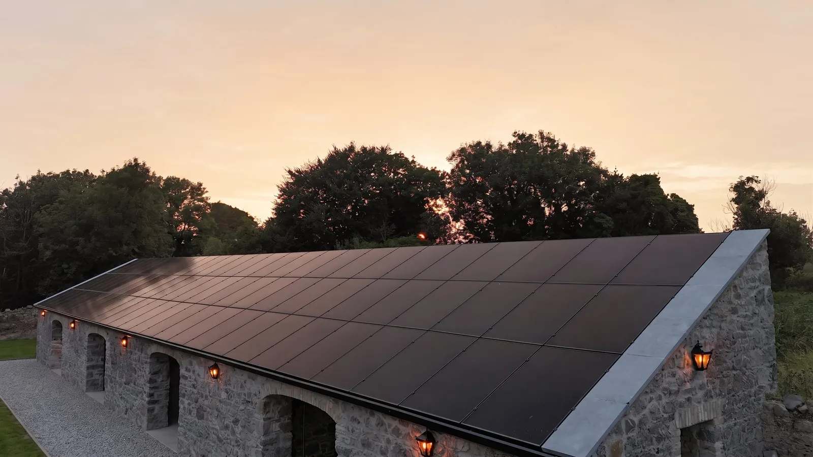 In-roof solar panels on a restored stone outbuilding near Athlone at sunset, lanterns glowing on the walls